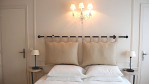 A neatly made bed with two pillows, a bedside table with a lamp, and a wall-mounted light fixture. - La Villa Paris (Paris)
