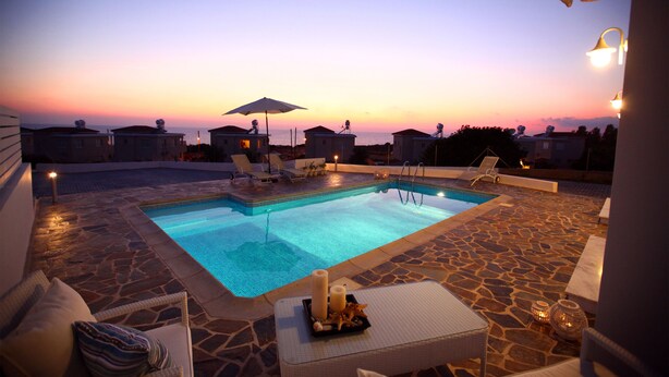 Une piscine dotée de chaises longues et d’un parasol, entourée d’un sol en pierre et offrant une vue sur le coucher de soleil.