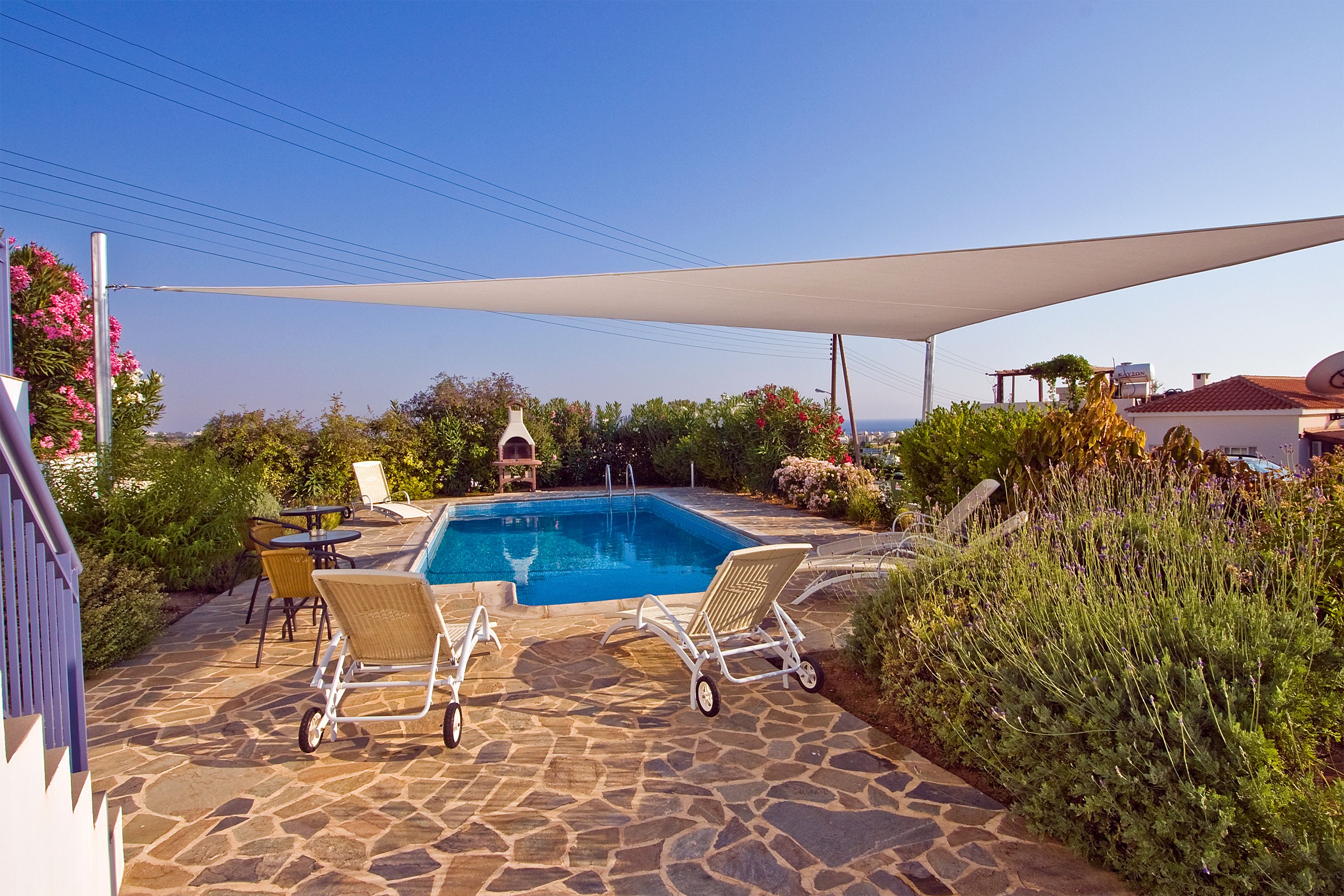 A pool area with stone flooring, two lounge chairs, a table, and a canopy.