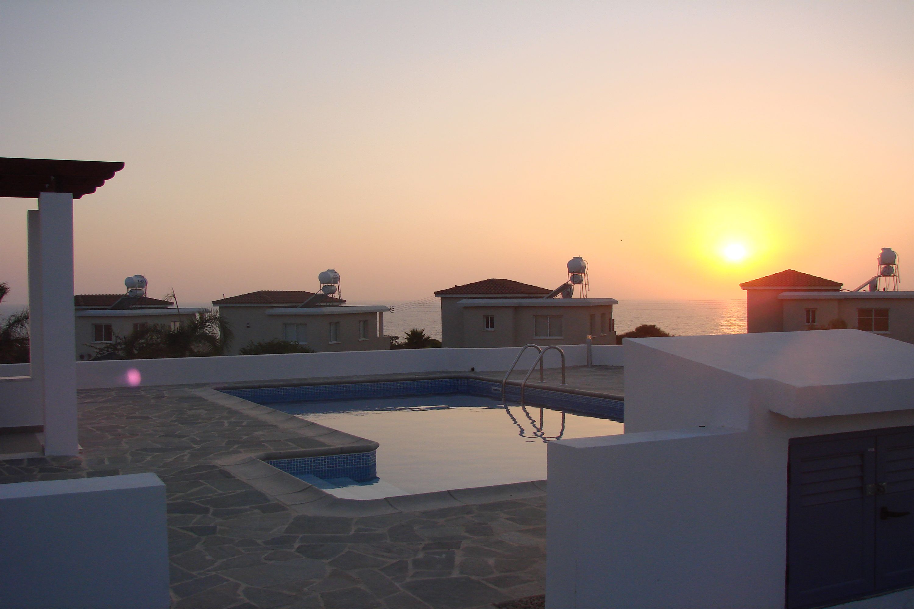 Una piscina sul tetto con vista sul tramonto sul mare, circondata da edifici con serbatoi in cima.