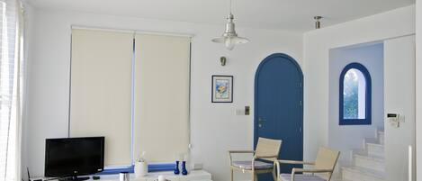A modern living room with a flat-screen TV, a glass coffee table, a sofa, and a blue door.