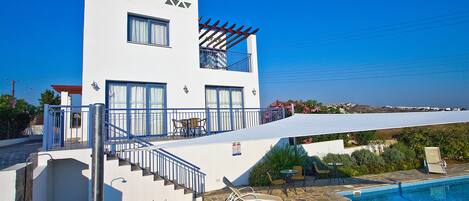 A modern building with a pool, outdoor seating, and a view of the sea.