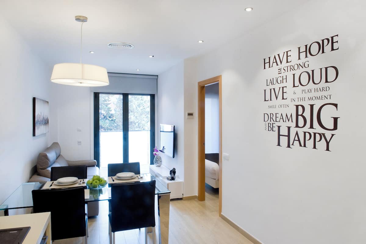 A modern living room with a dining area, a large window, and motivational wall art.