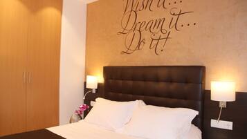 A neatly made bed with white linens, a dark headboard, and a motivational wall quote.