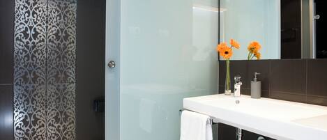 Un baño moderno con cabina de ducha de vidrio, un lavamanos blanco con espejo y un jarrón con flores.
