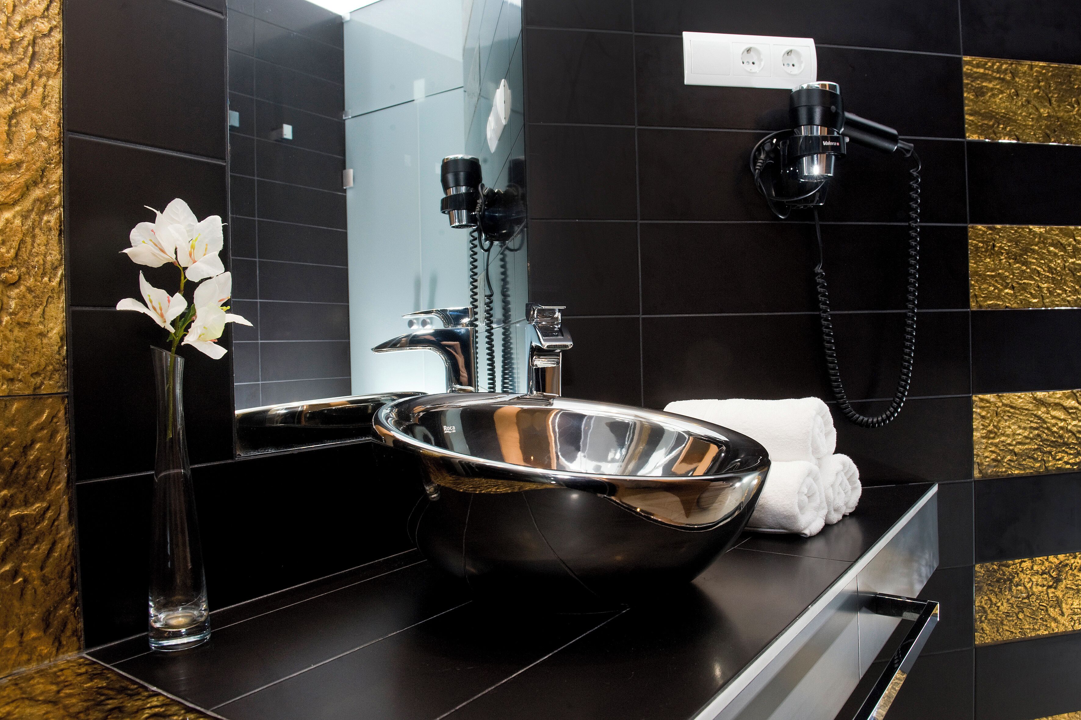 Une salle de bain moderne avec un lavabo noir, un vase en verre contenant des fleurs blanches et un porte-serviettes.
