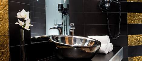 Une salle de bain moderne avec un lavabo noir, un vase en verre contenant des fleurs blanches et un porte-serviettes.