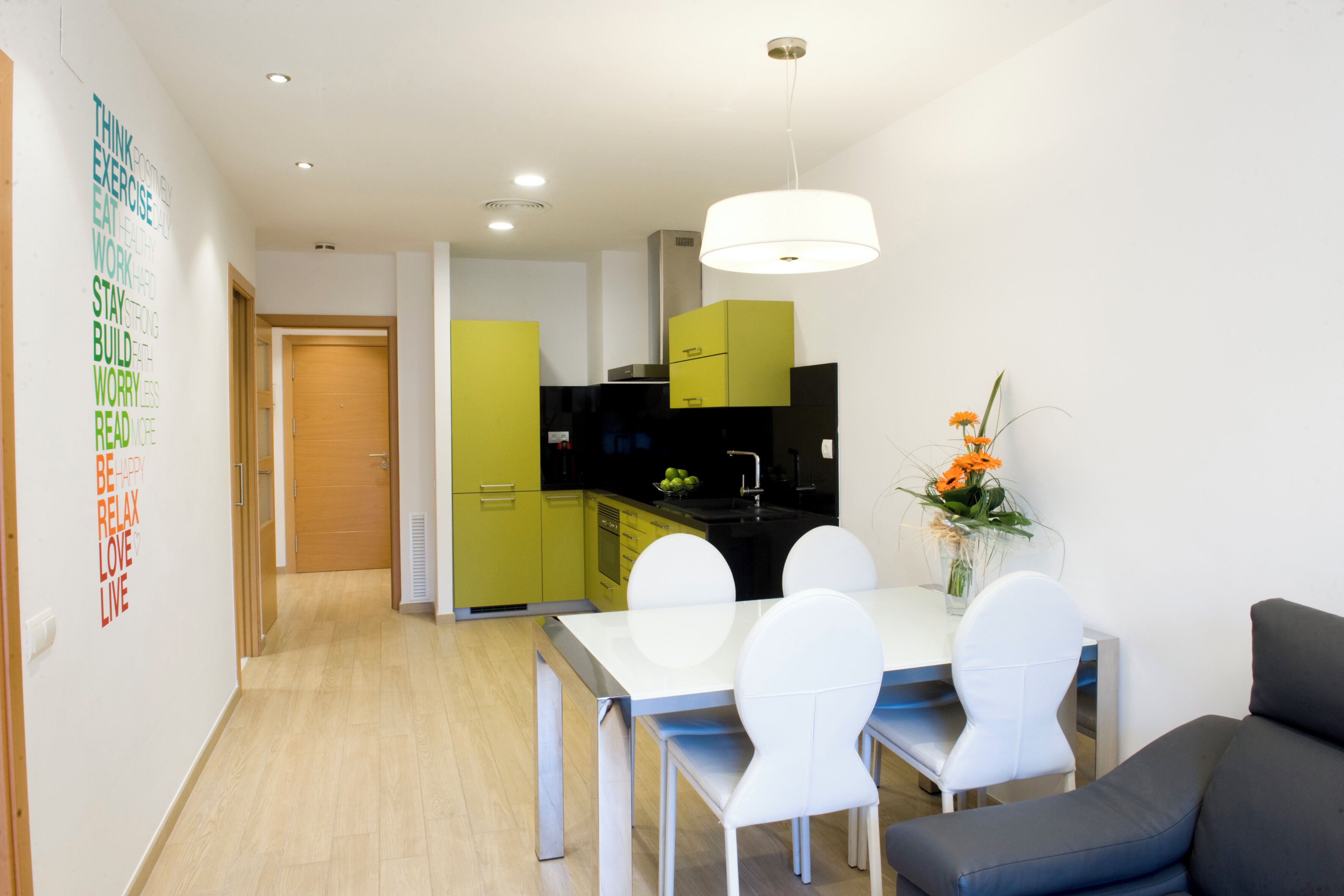 A modern kitchen with green cabinets, a white dining table with chairs, and a grey sofa.