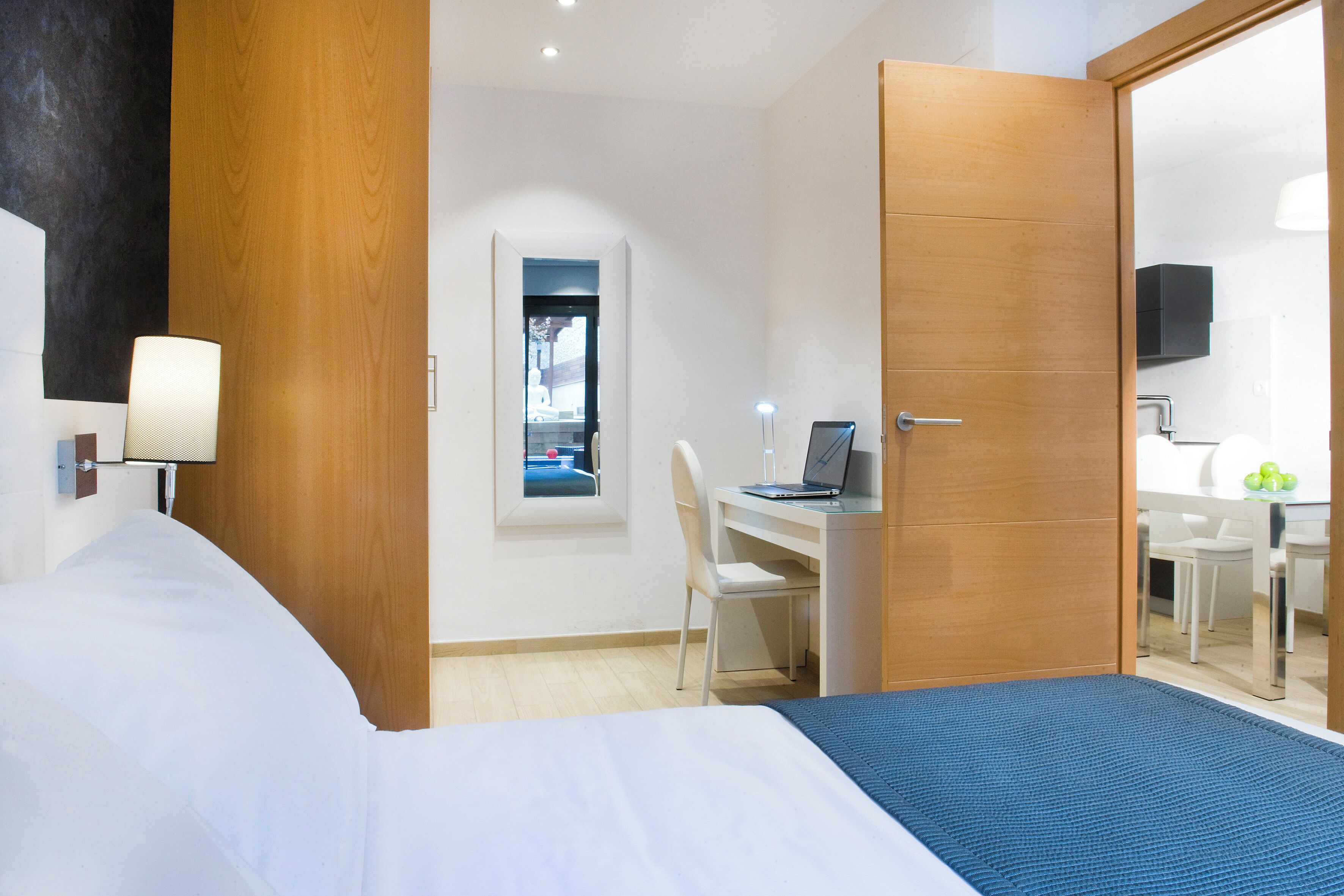 Una habitación de hotel con una cama, un escritorio con una computadora portátil, una silla y un espejo.