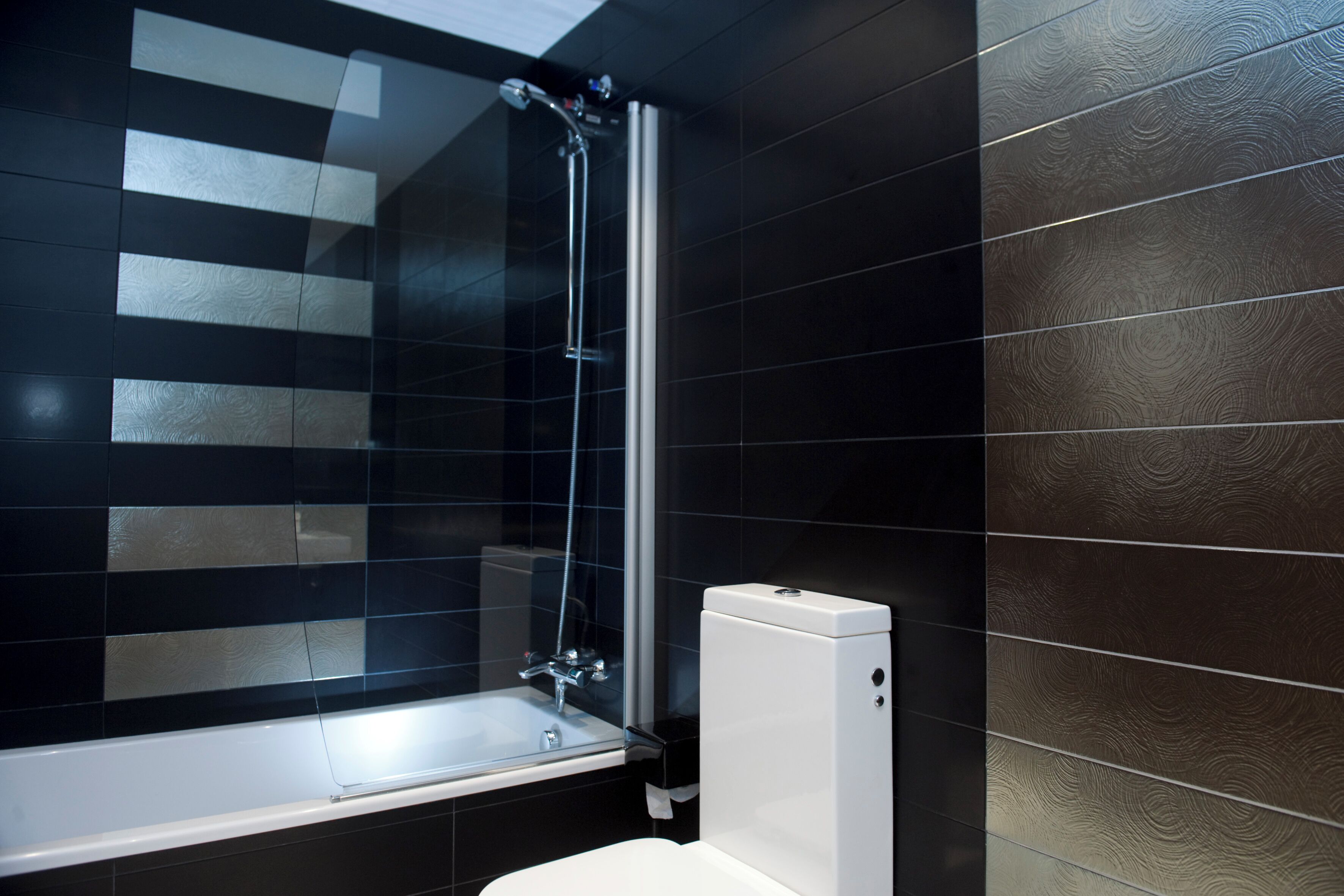 Une salle de bain moderne avec une douche à parois de verre, des toilettes blanches et des murs recouverts de carreaux foncés.