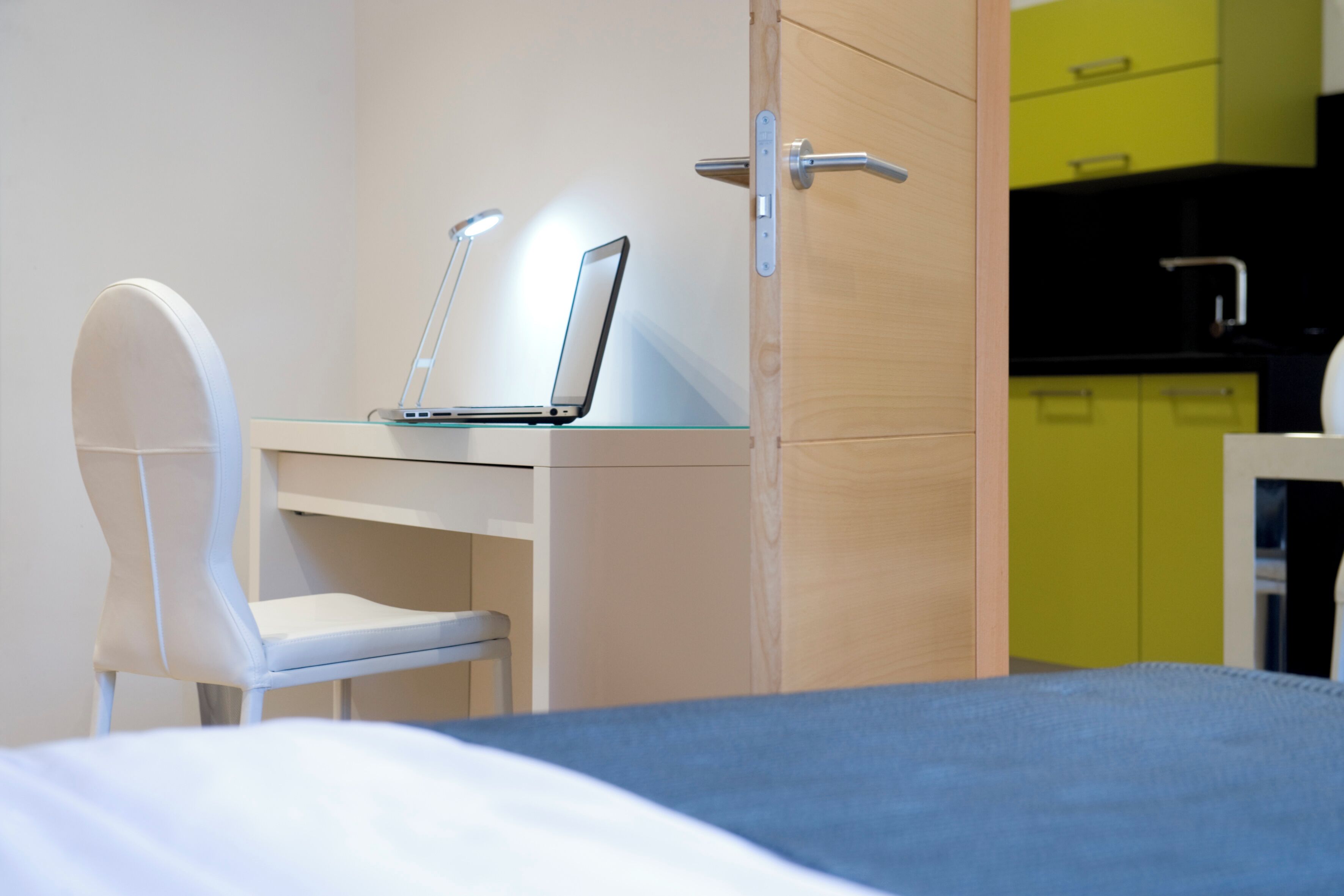 Une chambre d’hôtel moderne équipée d’un lit, d’un bureau avec un ordinateur portable, d’une chaise et d’un coin cuisine.