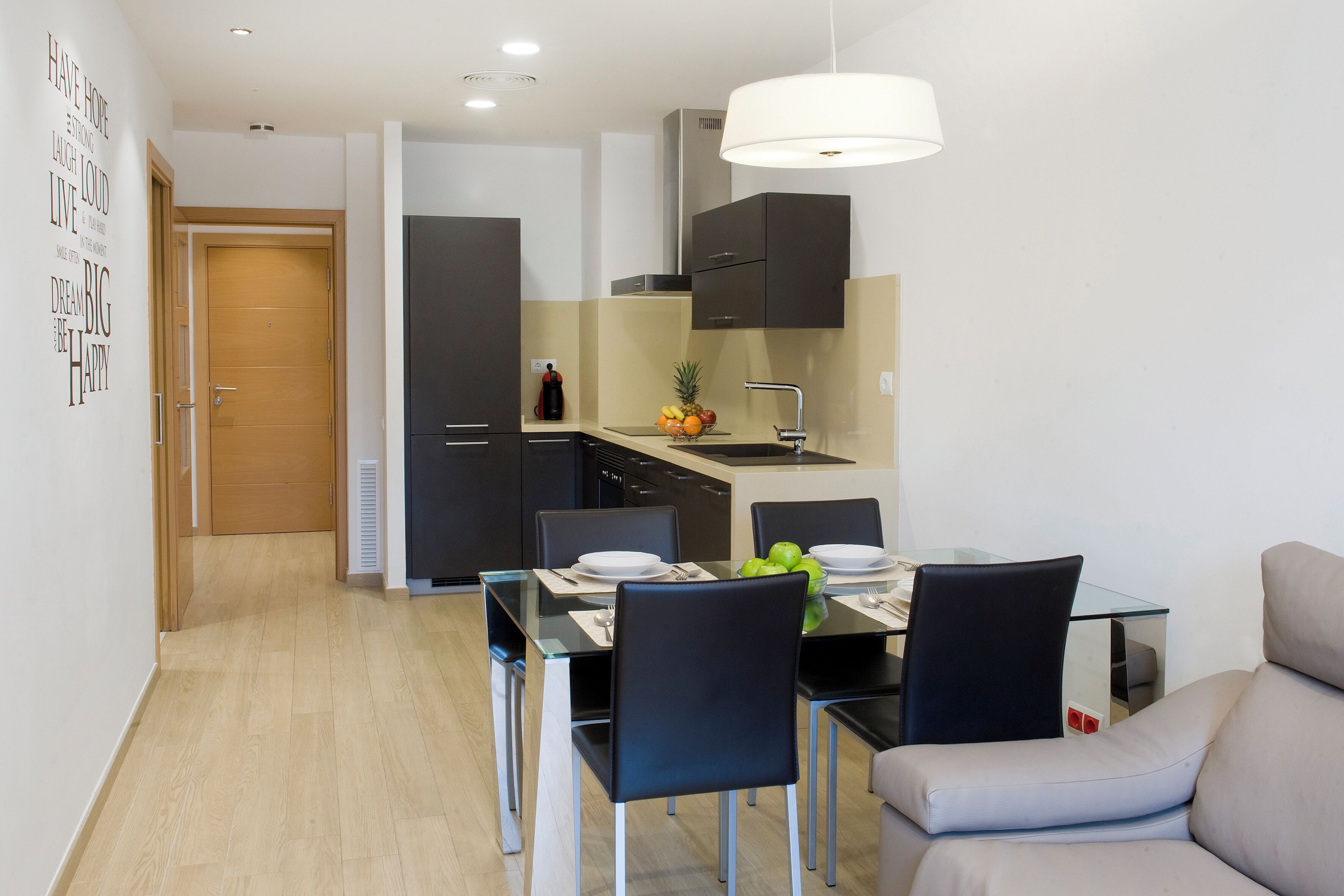 Una cocina moderna con zona de comedor, que incluye una mesa de vidrio, sillas negras y un sofá gris.
