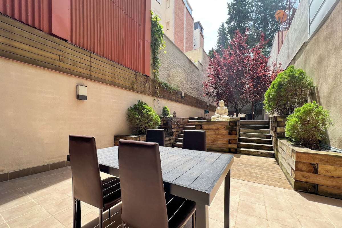 An outdoor patio with a table and chairs, surrounded by wooden planters and a statue.