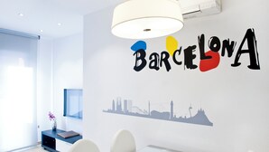 A modern dining area with a table and chairs, a vase with flowers, and a wall decal with the word "Barcelona" and a city skyline silhouette. - Home To Home Barcelona (Barcelona)