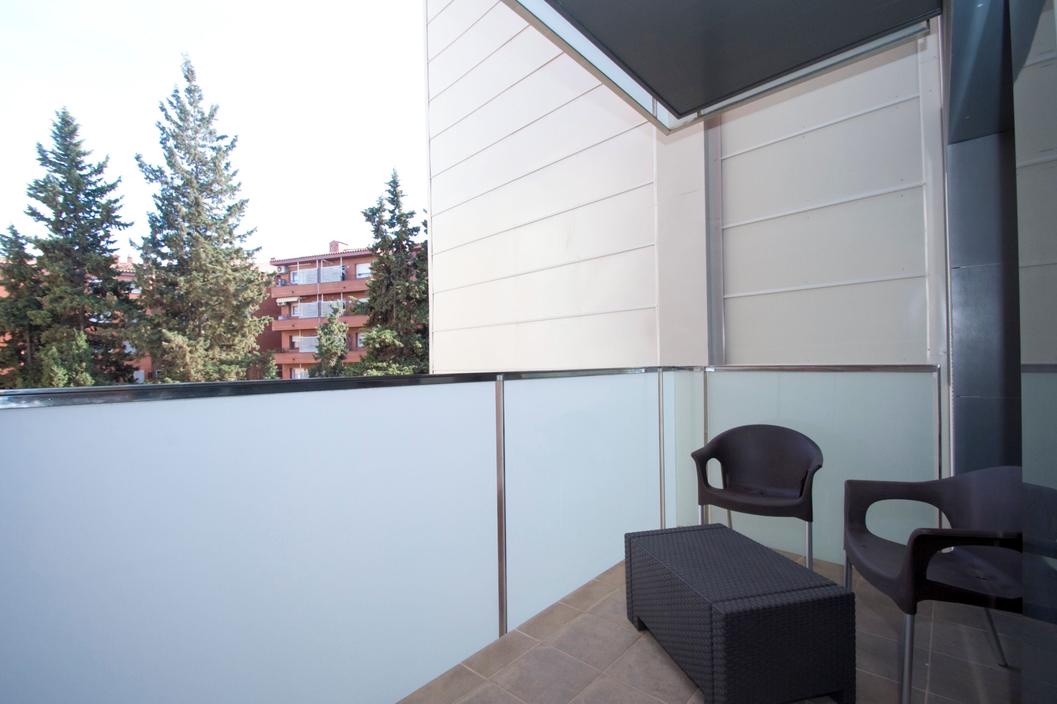 A balcony with a glass partition, two chairs, and a small table.