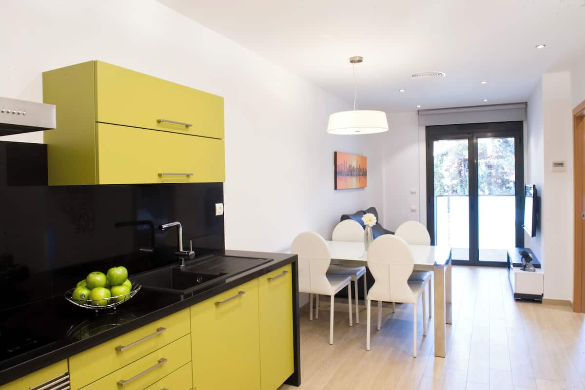 A modern kitchen with a black countertop, a yellow cabinet, and a bowl of green apples.