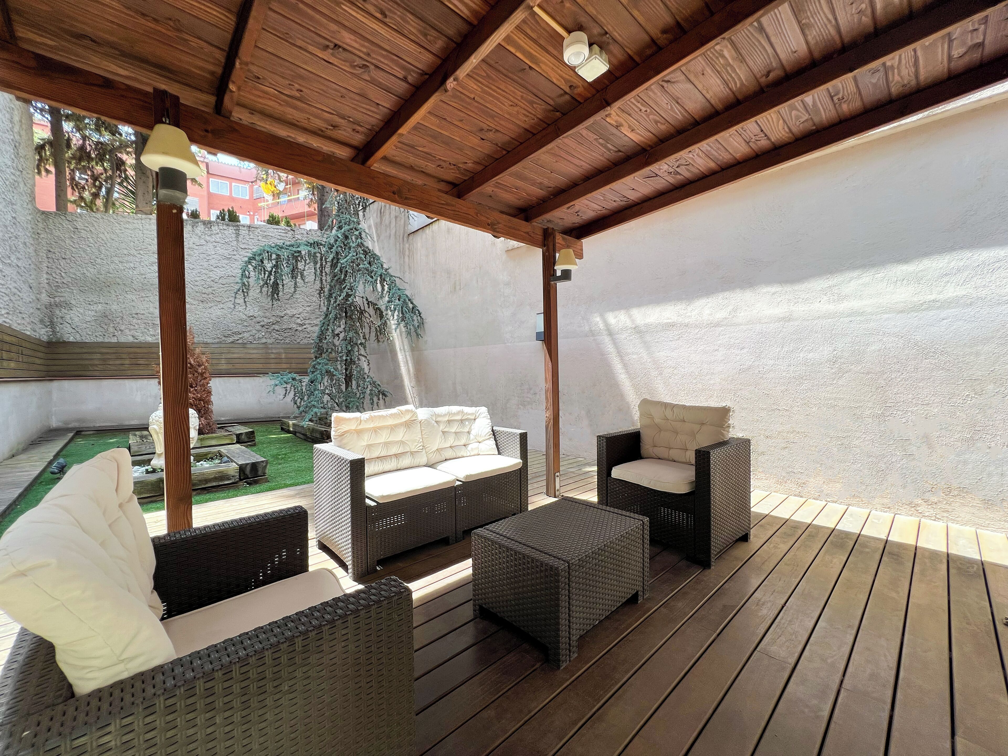 Un patio al aire libre con mobiliario de mimbre, techo de madera y vistas a un jardín.