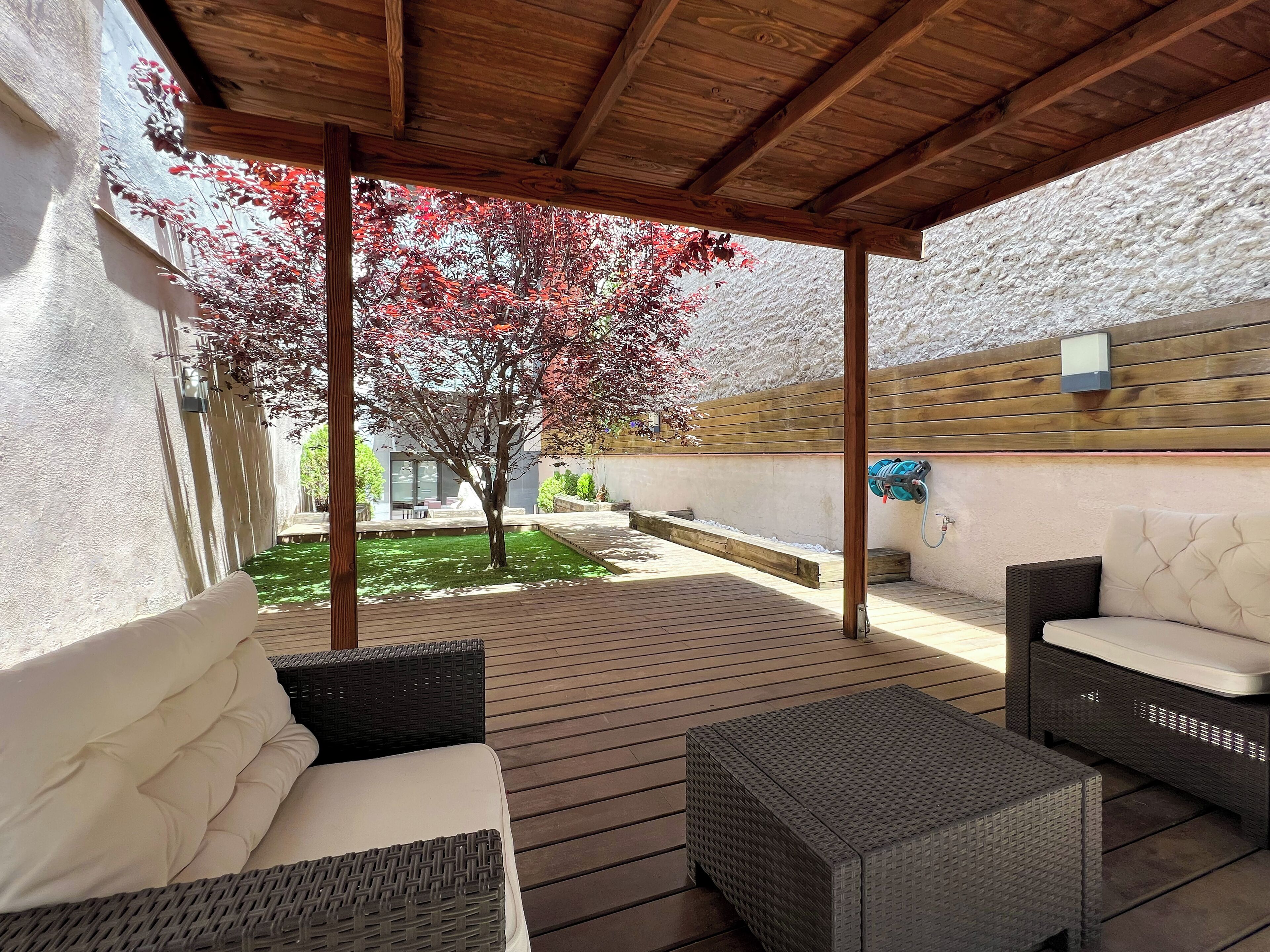 An outdoor patio area with a wooden ceiling, wicker furniture, and a tree with red leaves.