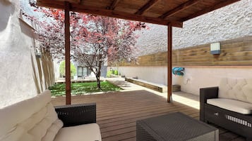 An outdoor patio area with a wooden ceiling, wicker furniture, and a tree with red leaves.