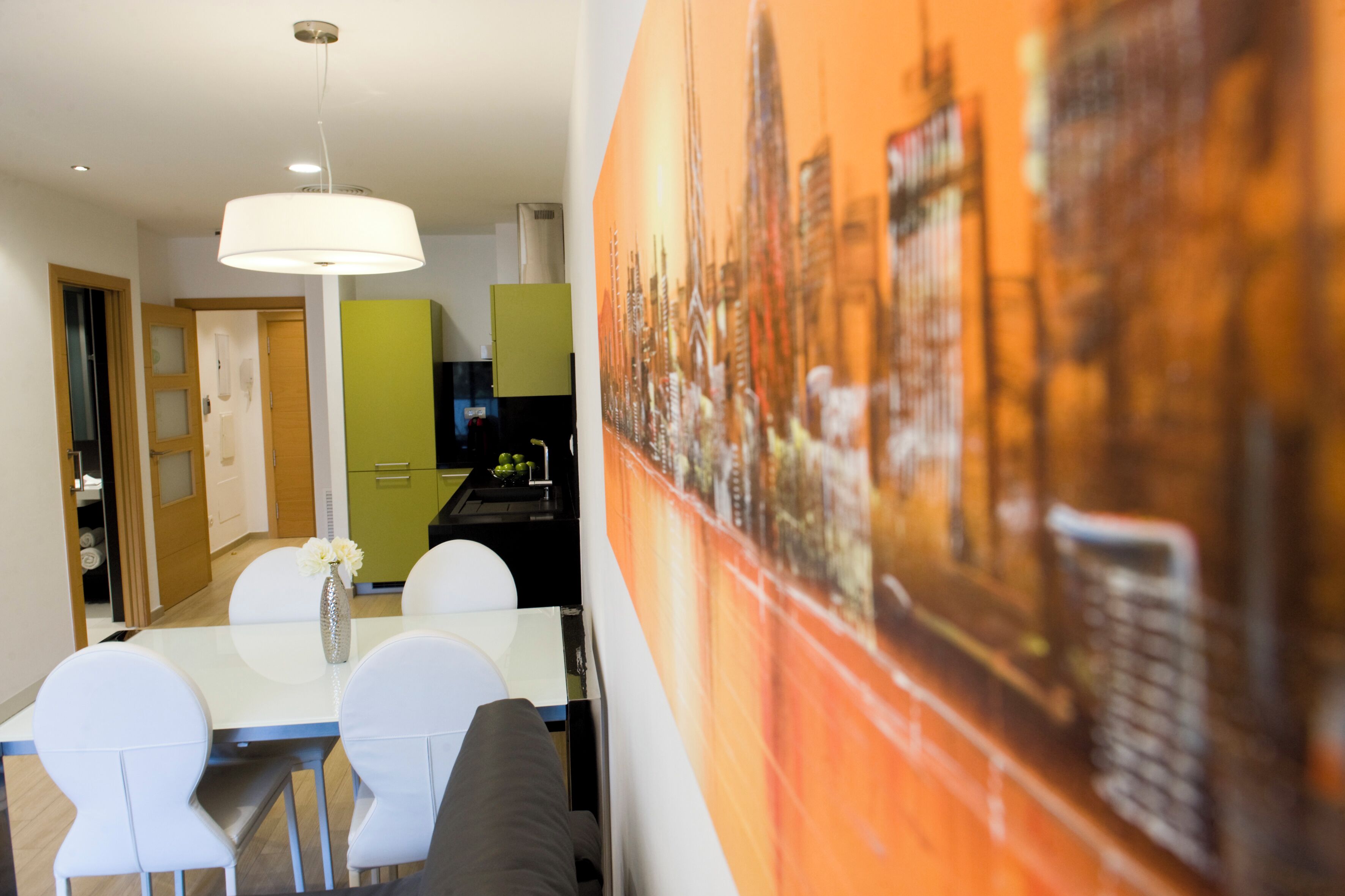 A modern kitchen with a dining area, a green cabinet, and a cityscape painting on the wall.