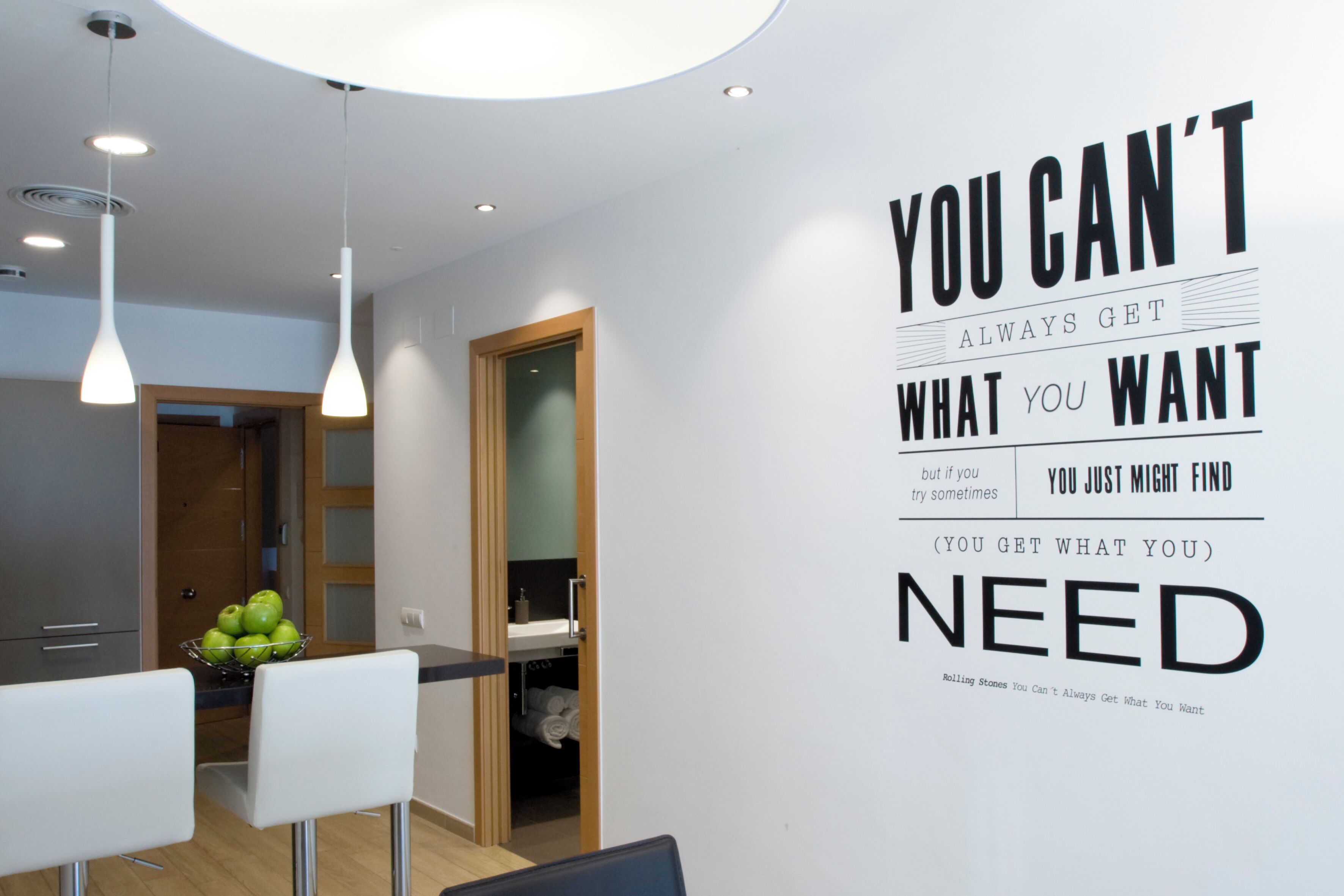 A modern interior with a motivational quote on the wall, a dining area with white chairs, and a visible bathroom.