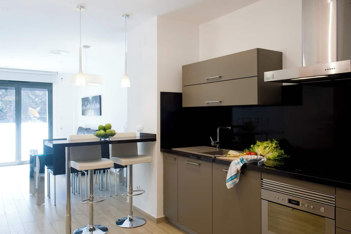 A modern kitchen with a black countertop, stainless steel appliances, and a dining area with bar stools.