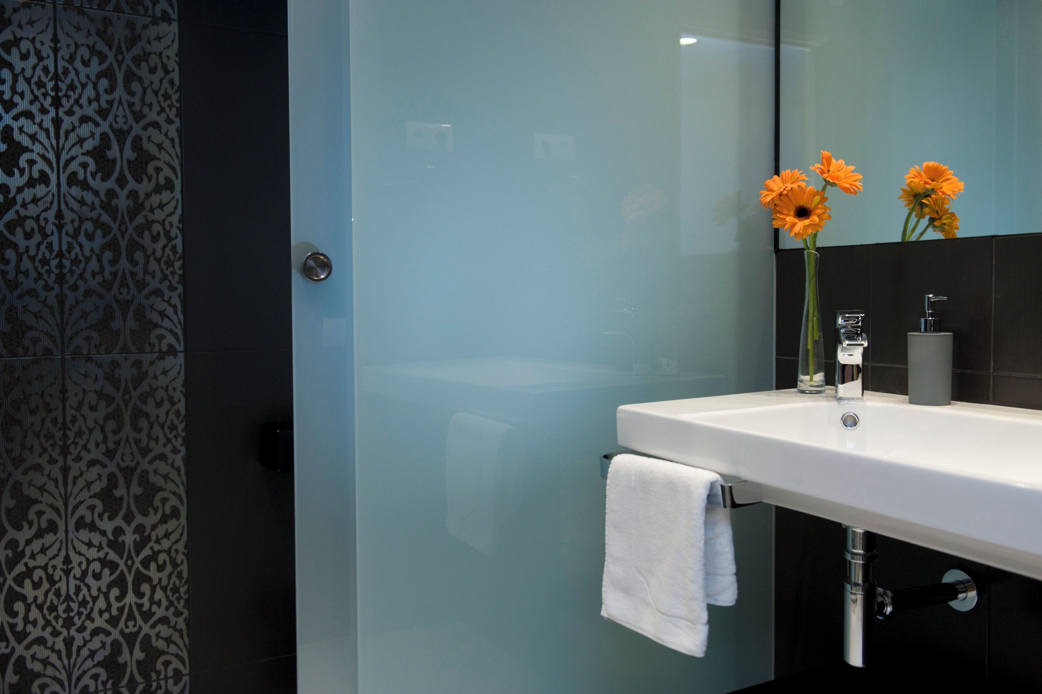 Un baño moderno con cabina de ducha de vidrio, un lavabo blanco con espejo y un florero con flores.