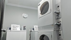 Una sala de lavandería con dos lavadoras y secadoras apiladas, un reloj en la pared y una puerta con picaporte plateado.
