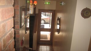 Un pasillo con pared de ladrillo, una puerta con ventana y suelo de baldosas.