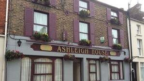 Un edificio con un letrero que dice "ASHLEIGH HOUSE" y varias ventanas con contraventanas.