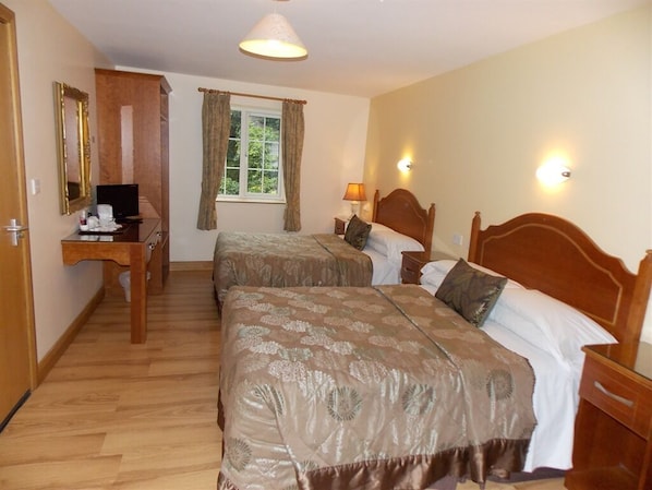 A hotel room with two beds, a desk with a computer, a window with curtains, and a lamp.