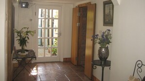 Un pasillo con suelo de baldosas, una puerta con paneles de vidrio, un ascensor de madera y una pequeña mesa con un jarrón de flores.
