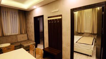 A hotel room with a sofa, a small table, a wooden bench, a bed with curtains, and a mirror.