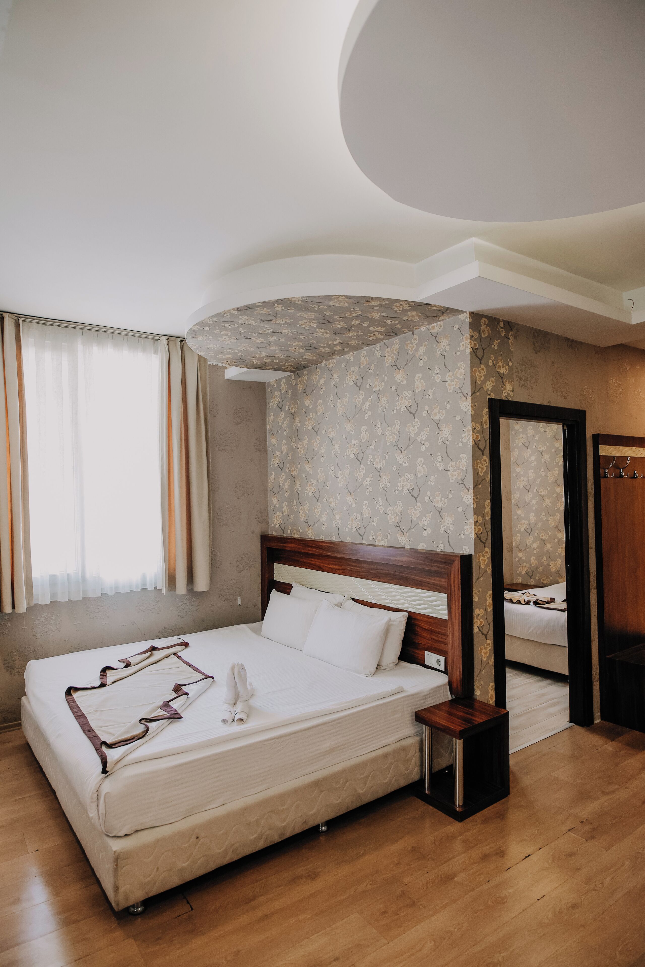 A bedroom with a large bed, a wooden headboard, a nightstand, a mirror, and a wardrobe.