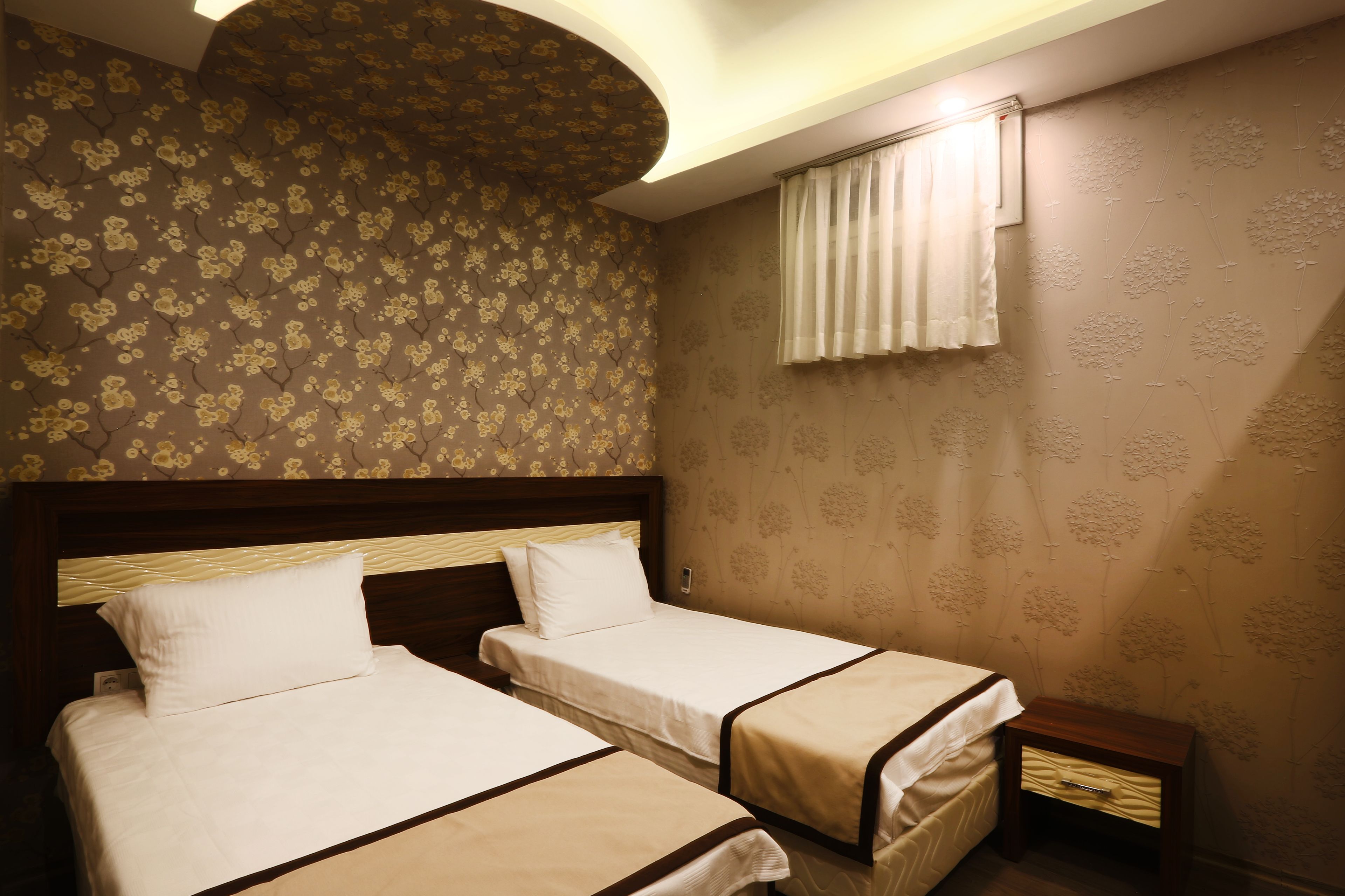 A hotel room with two beds, a small bedside table, and floral wallpaper.