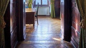 Una habitación con suelo de espiga, un escritorio de madera y una ventana con cortinas verdes.