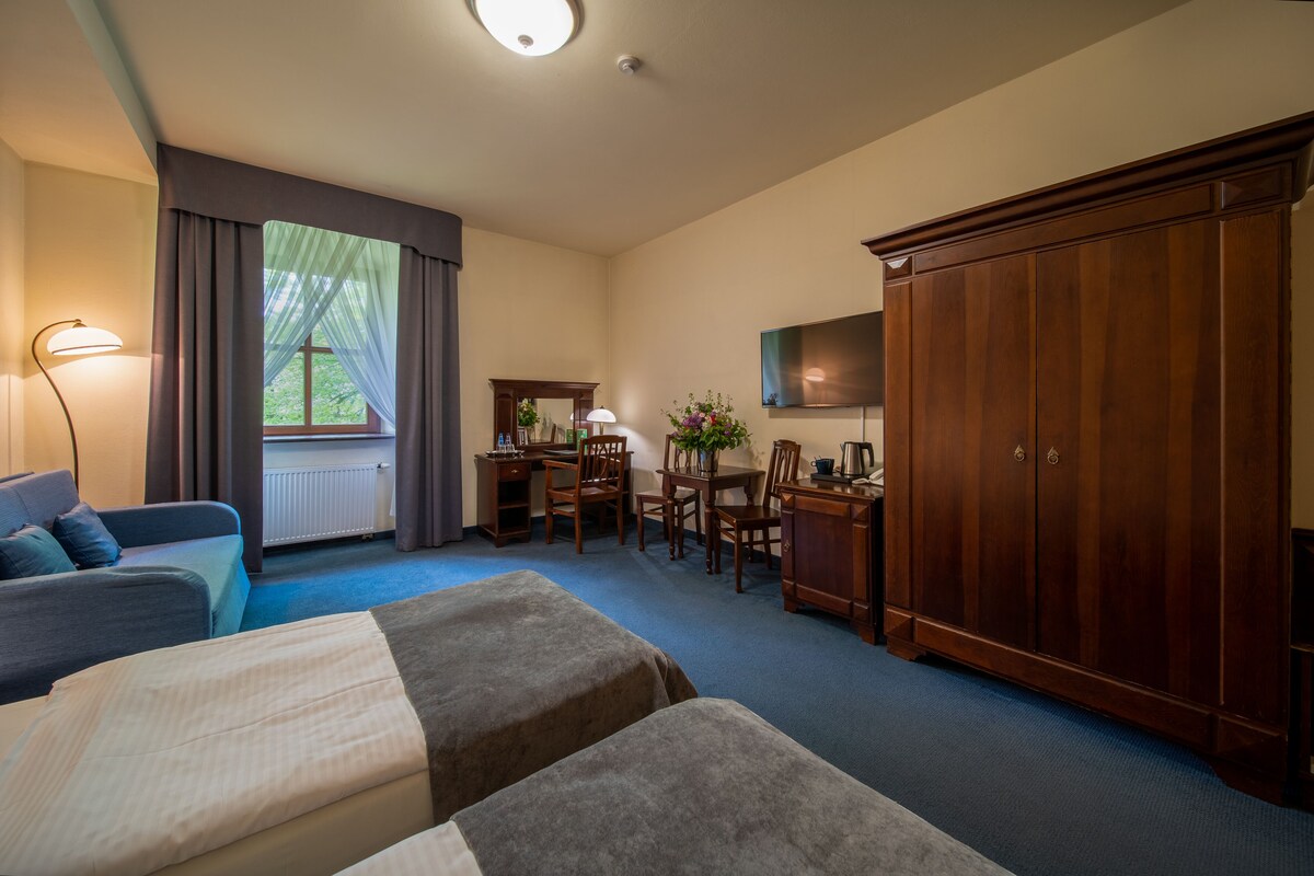 A hotel room with two beds, a desk, a chair, a wardrobe, and a television.