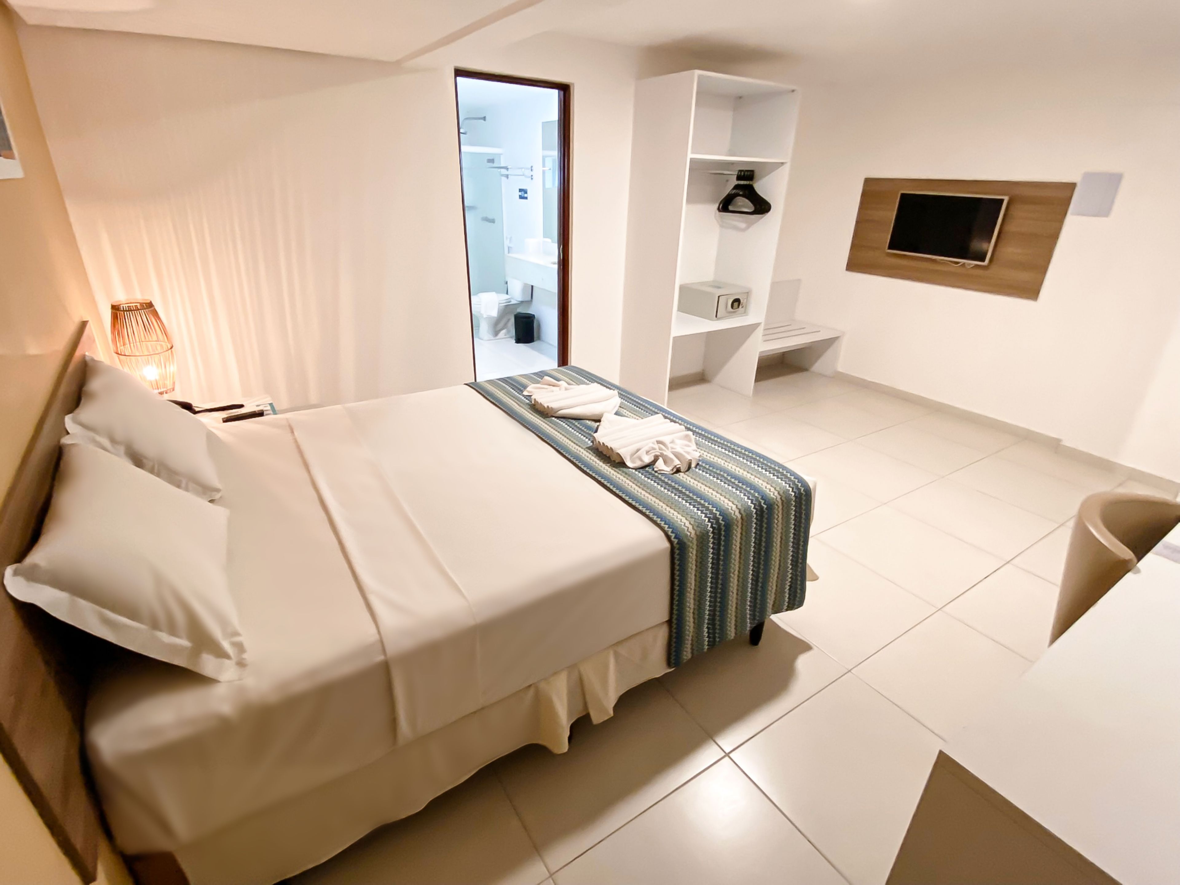 Una habitación de hotel con cama, mesita de noche, lámpara y vista al baño.