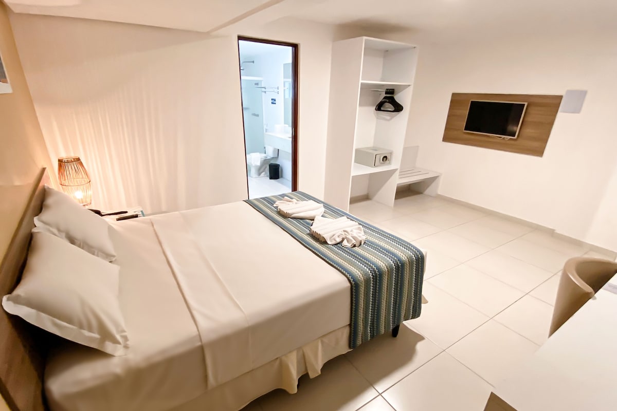 Ein Hotelzimmer mit Bett, Nachttisch, Lampe und Blick ins Badezimmer.