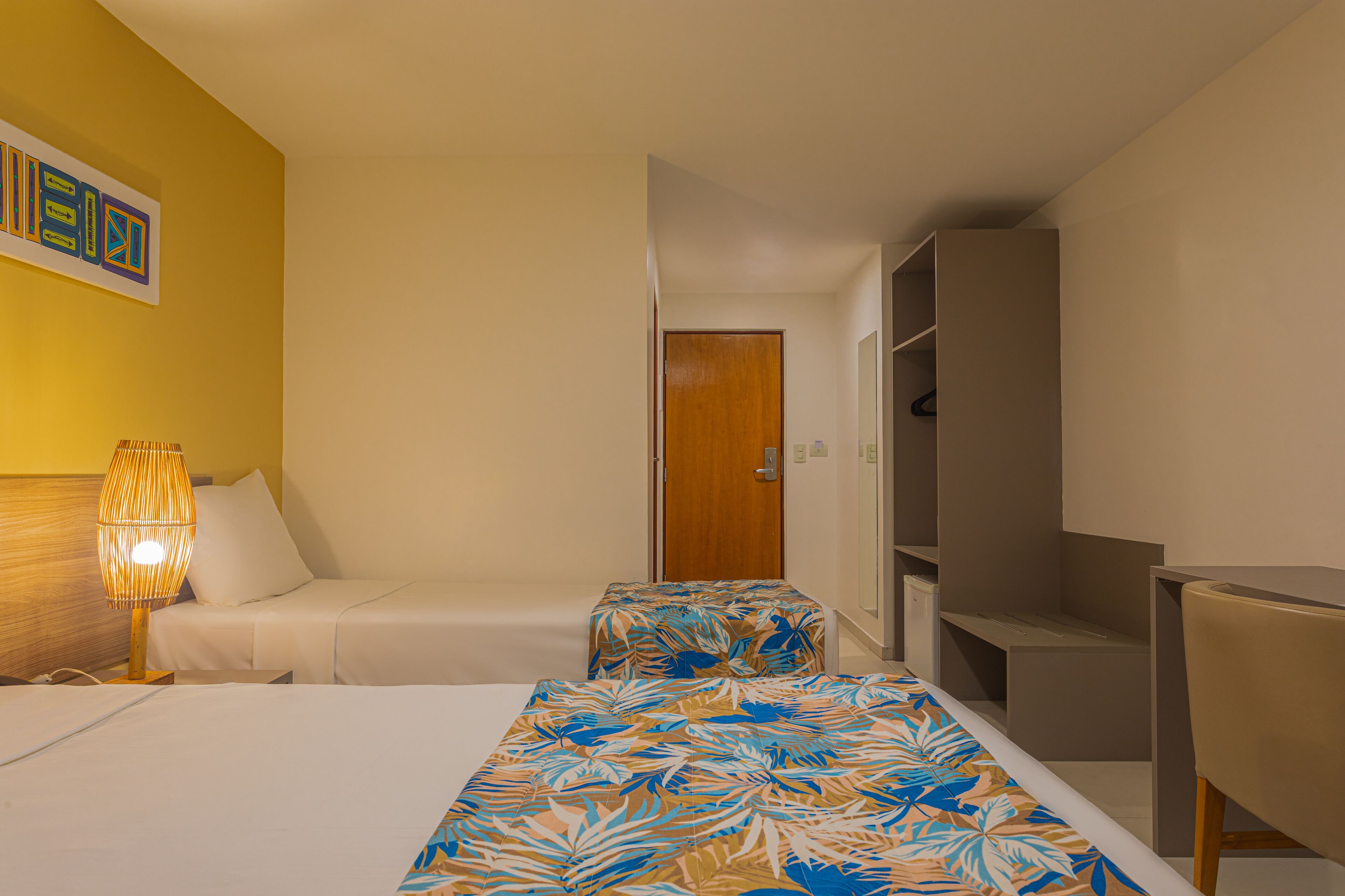 Habitación de hotel con cama, mesita de noche con lámpara, armario y escritorio.