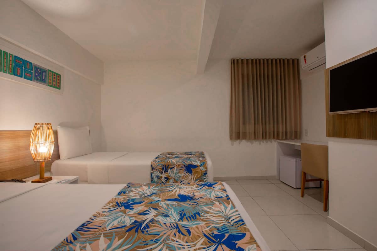 A hotel room with a bed, a desk, a chair, a lamp, and a TV.