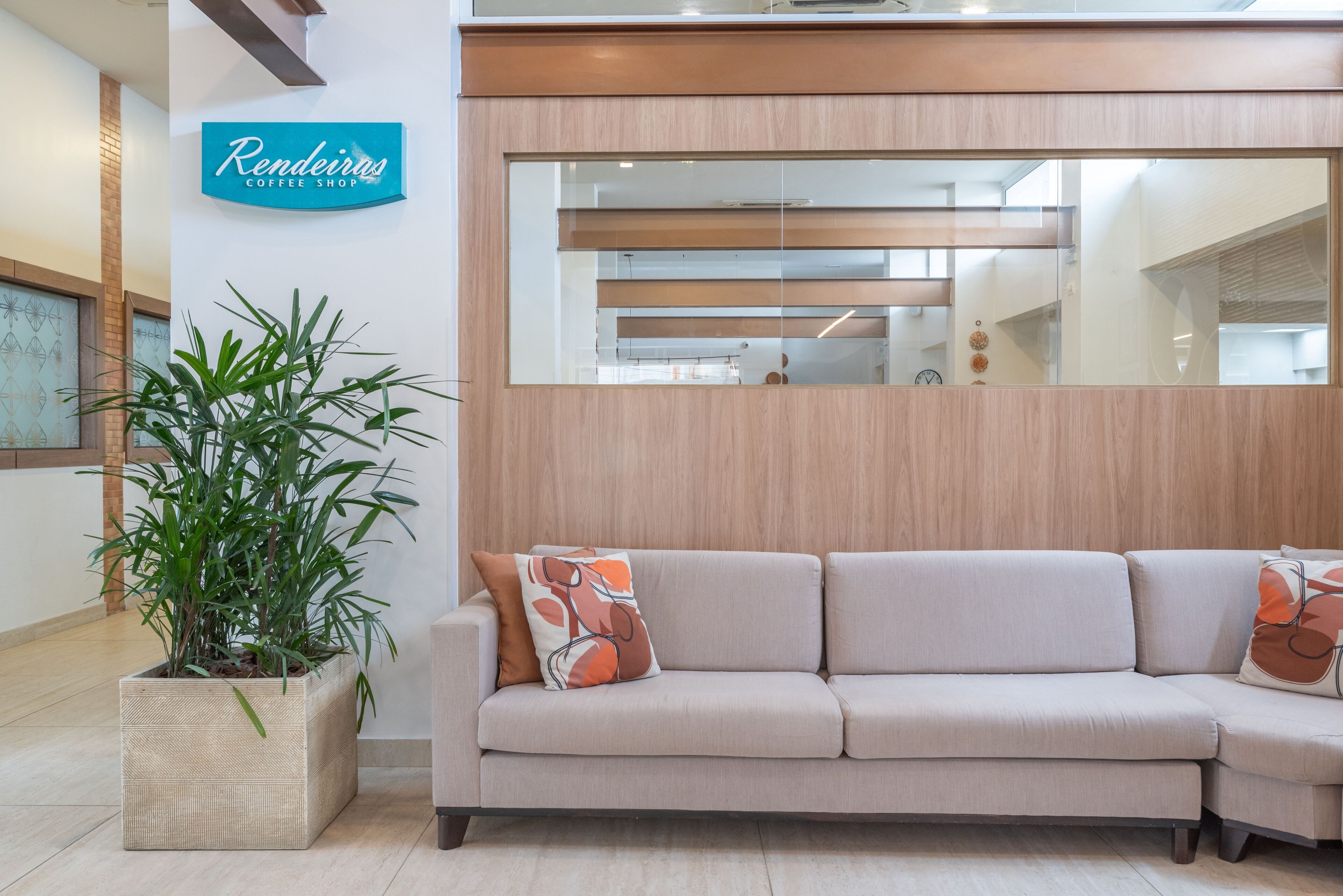 Un espace d’accueil avec un canapé beige, une plante en pot et un panneau indiquant le « Café Rendeiras ».