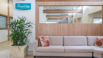 Un espace d’accueil avec un canapé beige, une plante en pot et un panneau indiquant le « Café Rendeiras ».