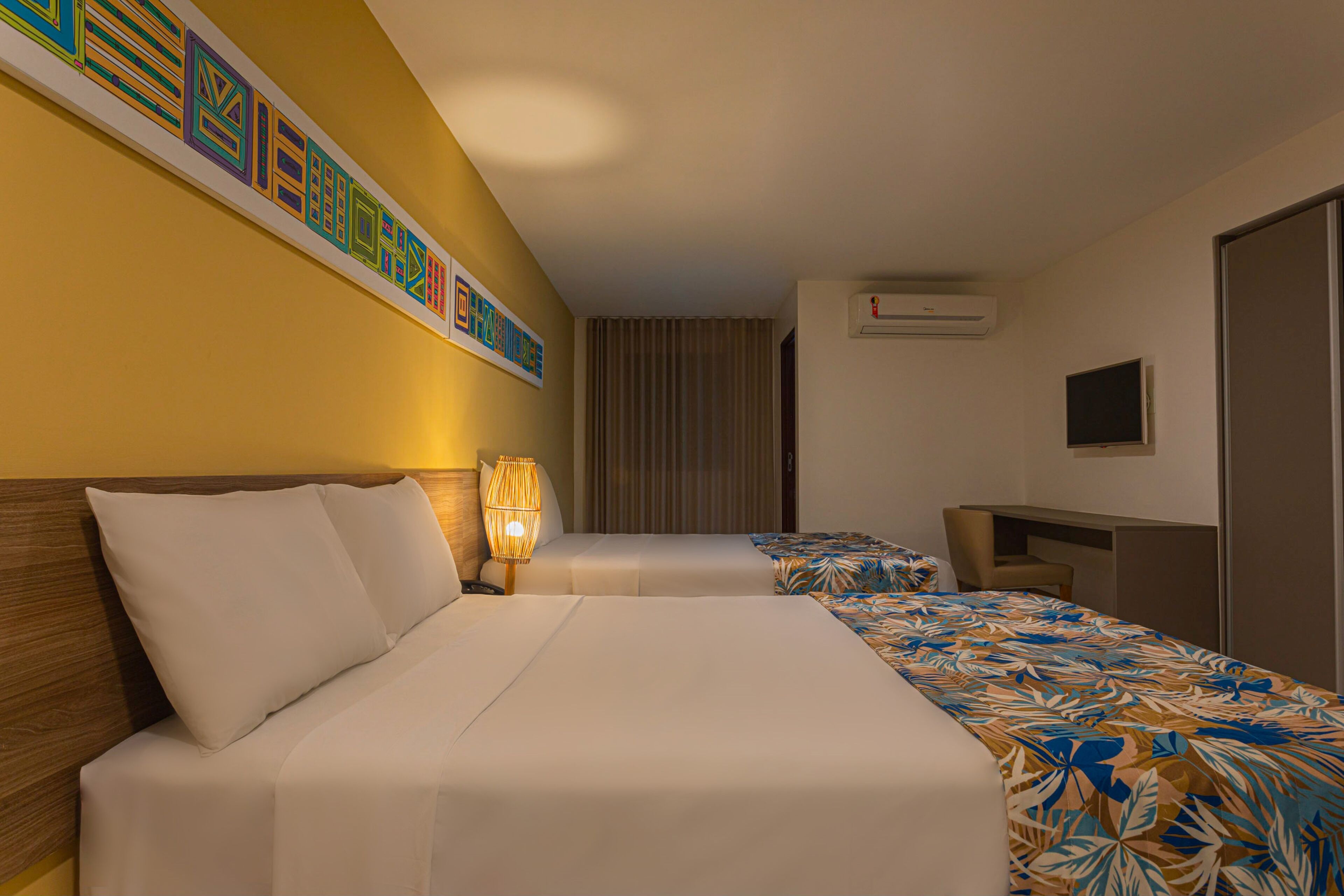 Een hotelkamer met twee bedden, een bureau, een lamp, een airconditioner en een decoratief wandobject.