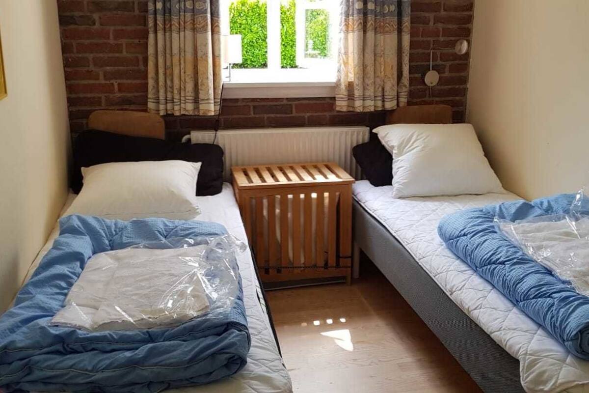 A small, cozy room with two single beds, a radiator, and a window with curtains.