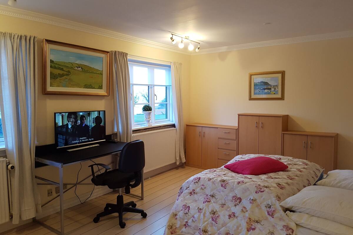 A bedroom with a bed, a desk with a chair, a television, and a window with curtains.