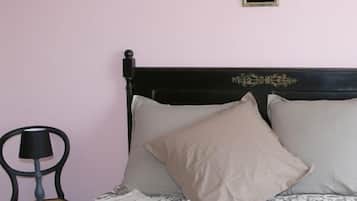 A bed with a dark wooden headboard, two beige pillows, and a lace-patterned bedspread. A chair with a black lamp is positioned to the left of the bed.
