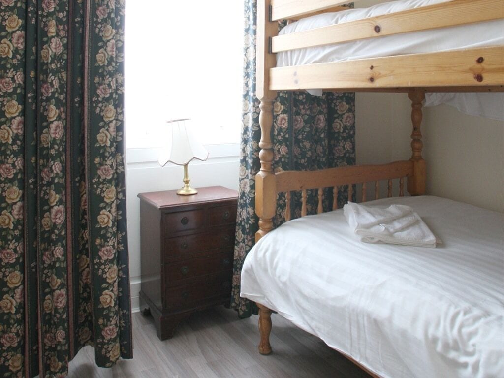 Une chambre avec un lit superposé en bois, une table de chevet avec une lampe et des rideaux à motifs floraux.