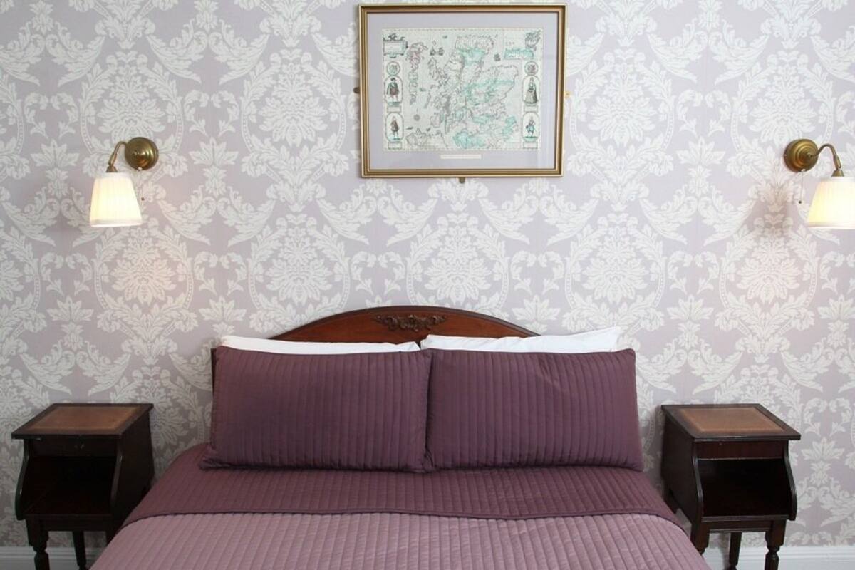 Ein Schlafzimmer mit einem großen Bett, zwei Nachttischen, einer gerahmten Karte an der Wand und Wandleuchten.