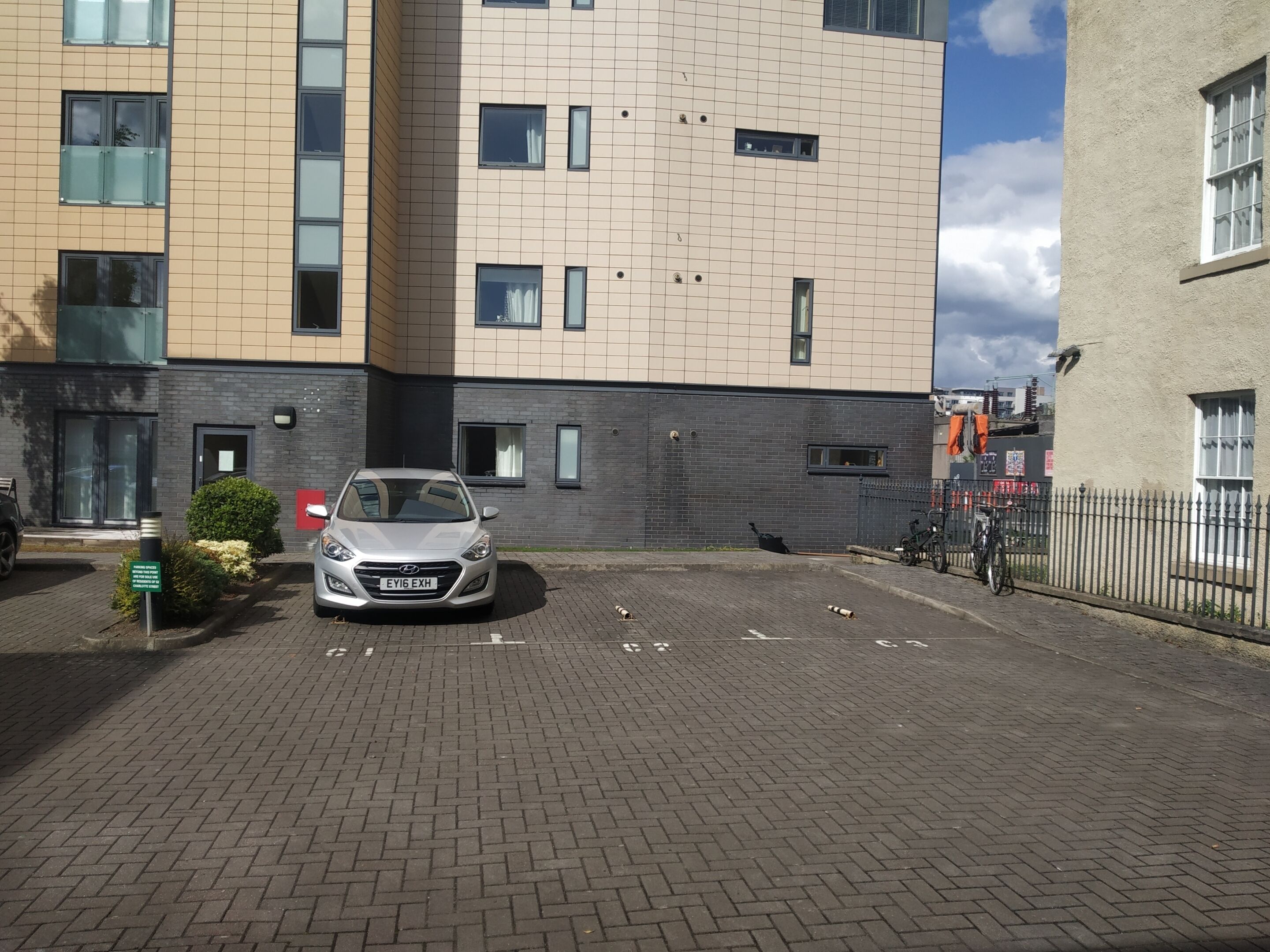 A parking area with a car, a building with multiple windows, and a paved walkway.